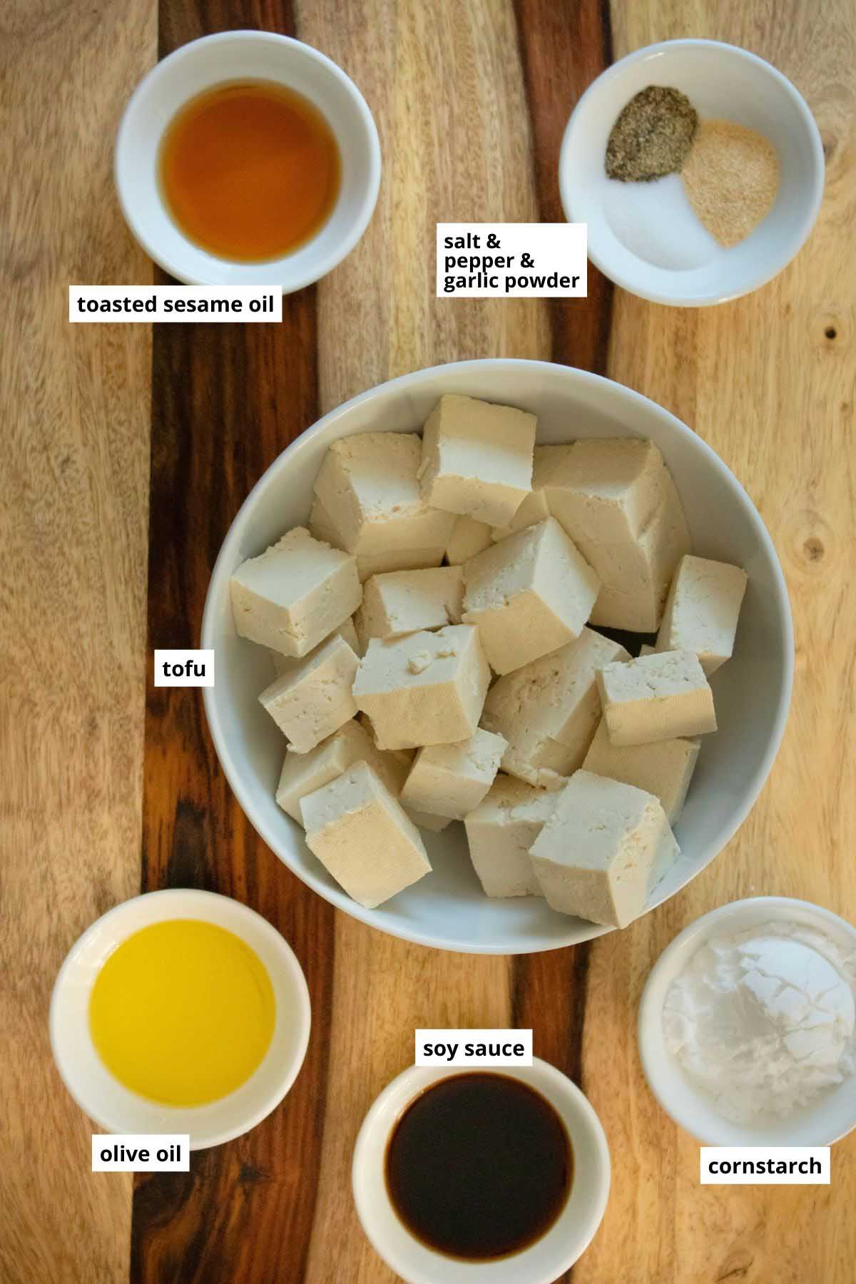 tofu, oils, spices, and soy sauce in bowls on a wooden cutting board