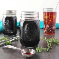 jars of instant pot elderberry syrup with a drink made from the syrup in the background