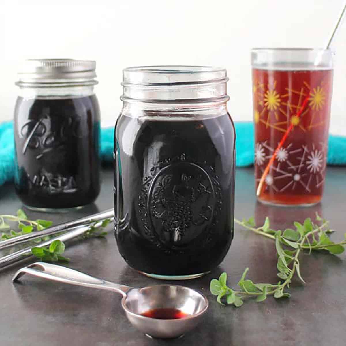 jars of instant pot elderberry syrup with a drink made from the syrup in the background