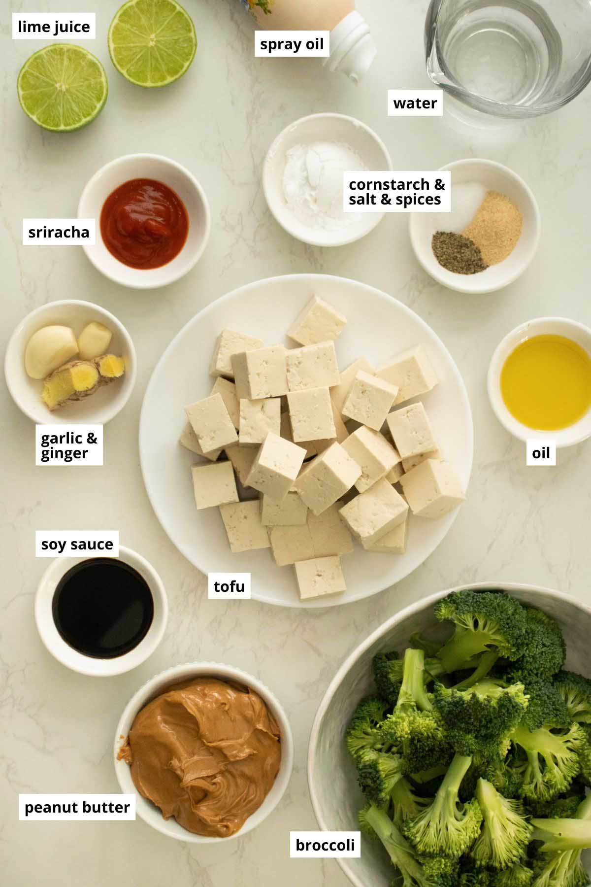 tofu, broccoli, and peanut sauce ingredients in bowls on a white table