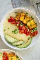 vegan grits bowls with tofu, avocado, tomato, and green onions in bowls on a white table