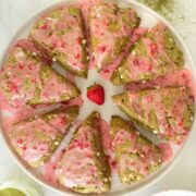 vegan matcha scones with strawberry glaze on a serving tray with matcha, glaze, and berries on the table around them