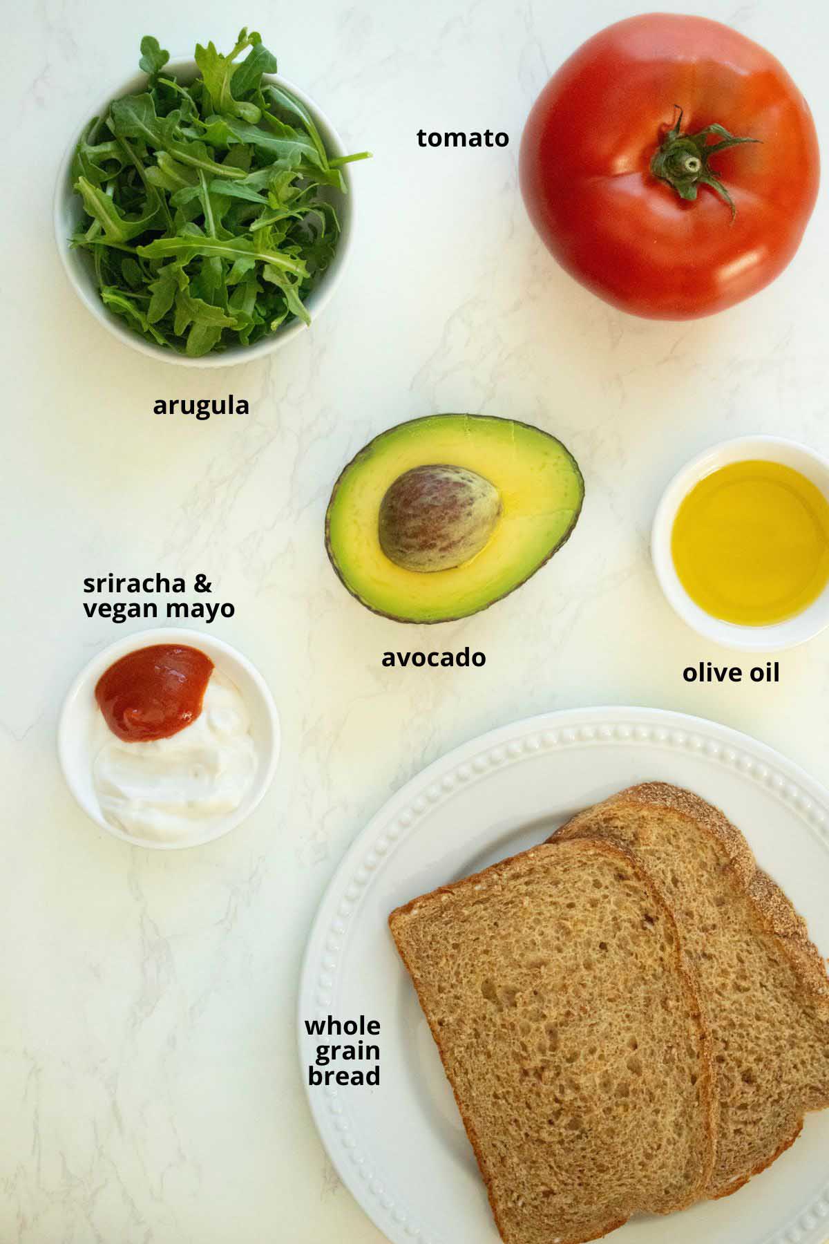 avocado, sriracha, mayo, bread, and other sandwich ingredients in bowls on a white table