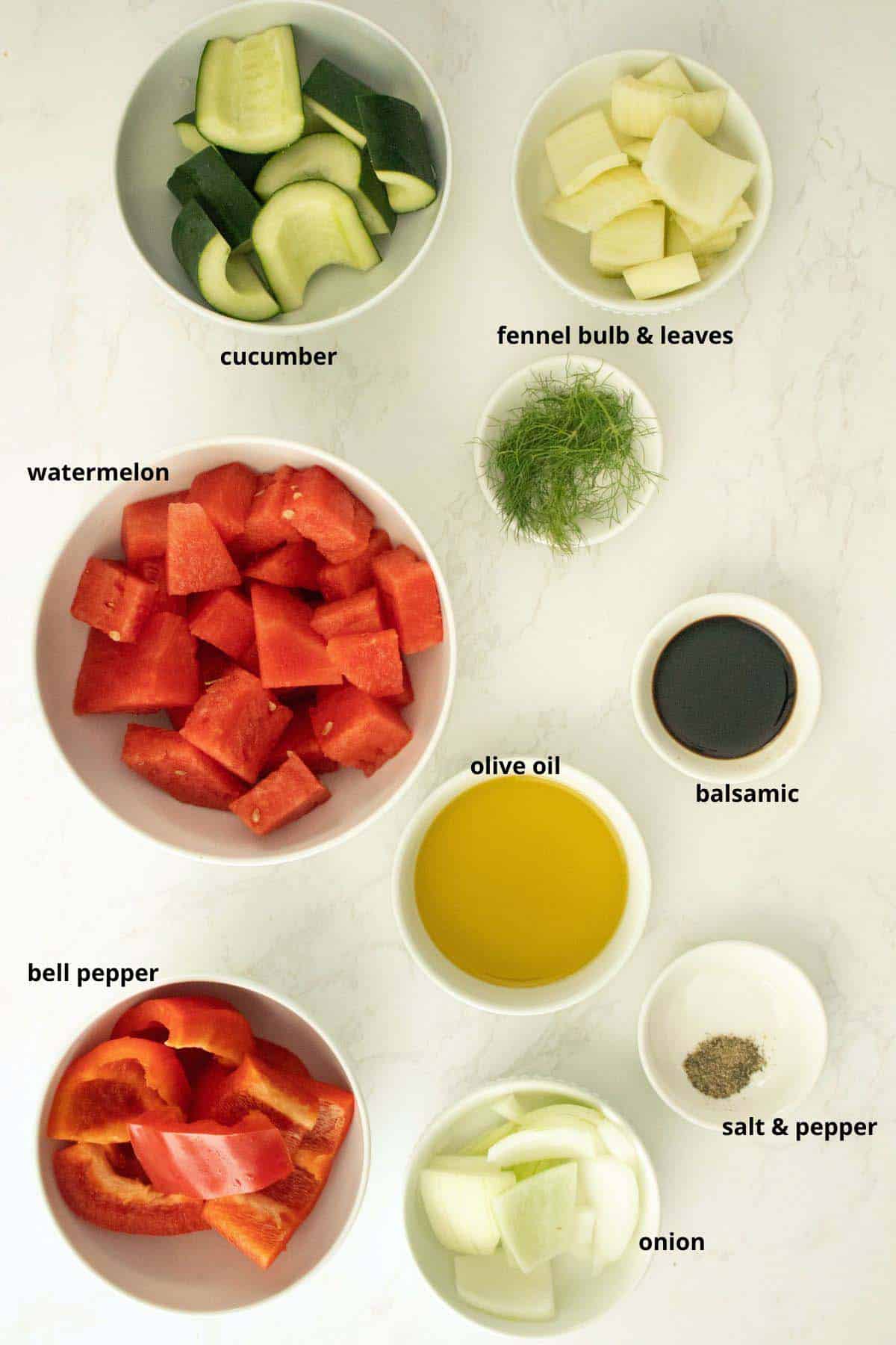 watermelon, fennel, cucumber, and other gazpacho ingredients in bowls on a white table
