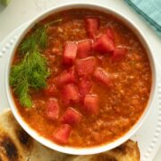 bowl of watermelon gazpacho topped with fennel leaves and chopped watermelon next to a side of toasted bread