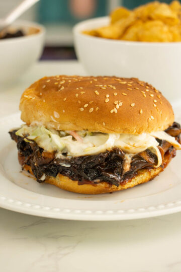 mushroom pulled pork sandwich with slaw on a white plate with sides in the background