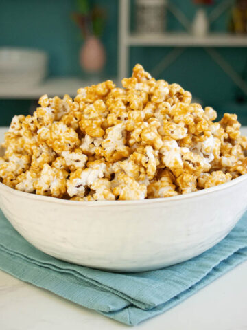 bowl of peanut butter popcorn on a blue napkin with kitchen shelves in the background