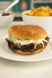 pulled mushroom sandwich with slaw on a sesame seed bun with chips in the background
