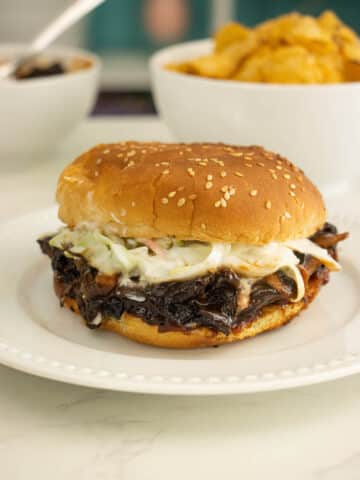 pulled mushroom sandwich with slaw on a sesame seed bun with chips in the background