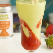 matcha milkshake with strawberry puree layered in a glass with a straw