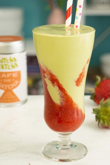 matcha milkshake with strawberry puree layered in a glass with a straw