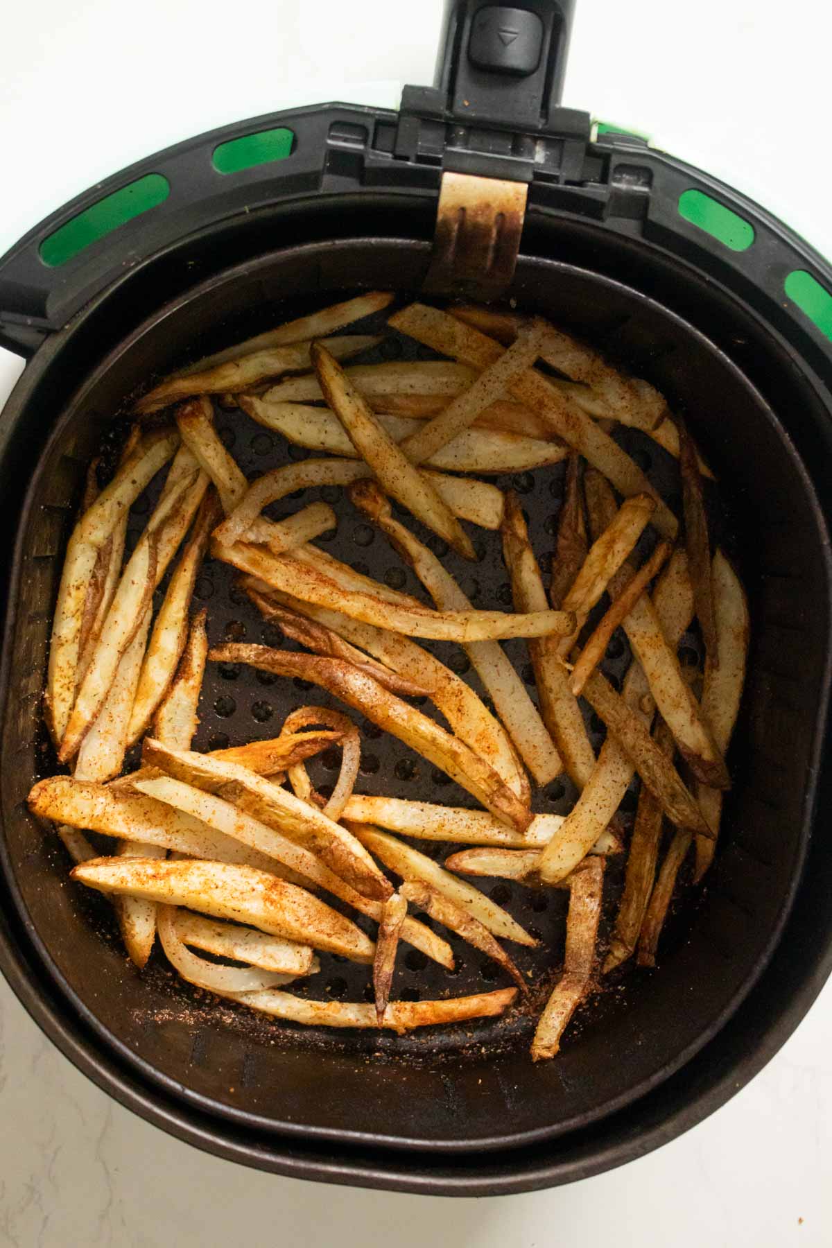 adding BBQ seasoning to the fries in the air fryer basket