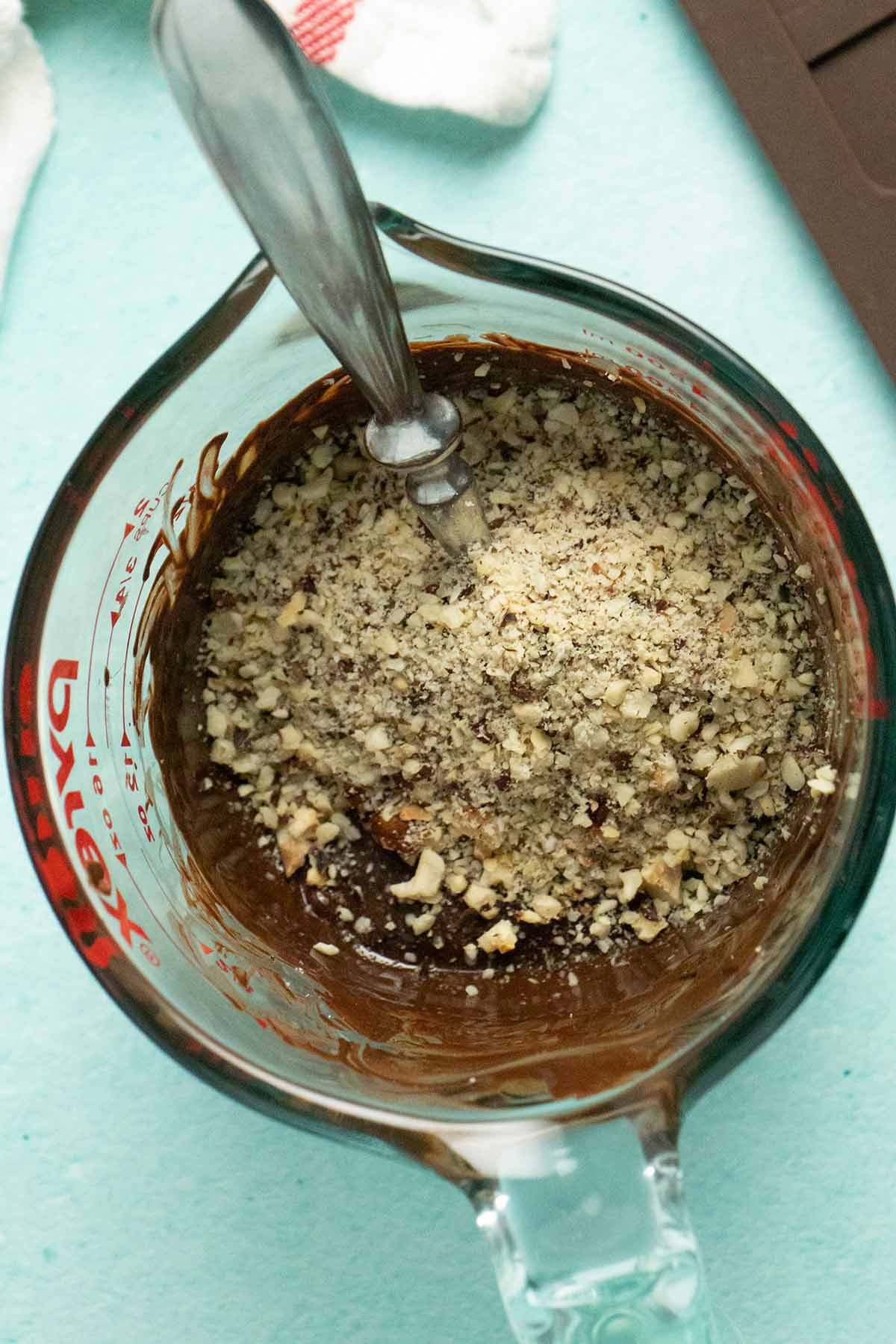 adding toasted hazelnuts to the melted chocolate in the measuring bowl