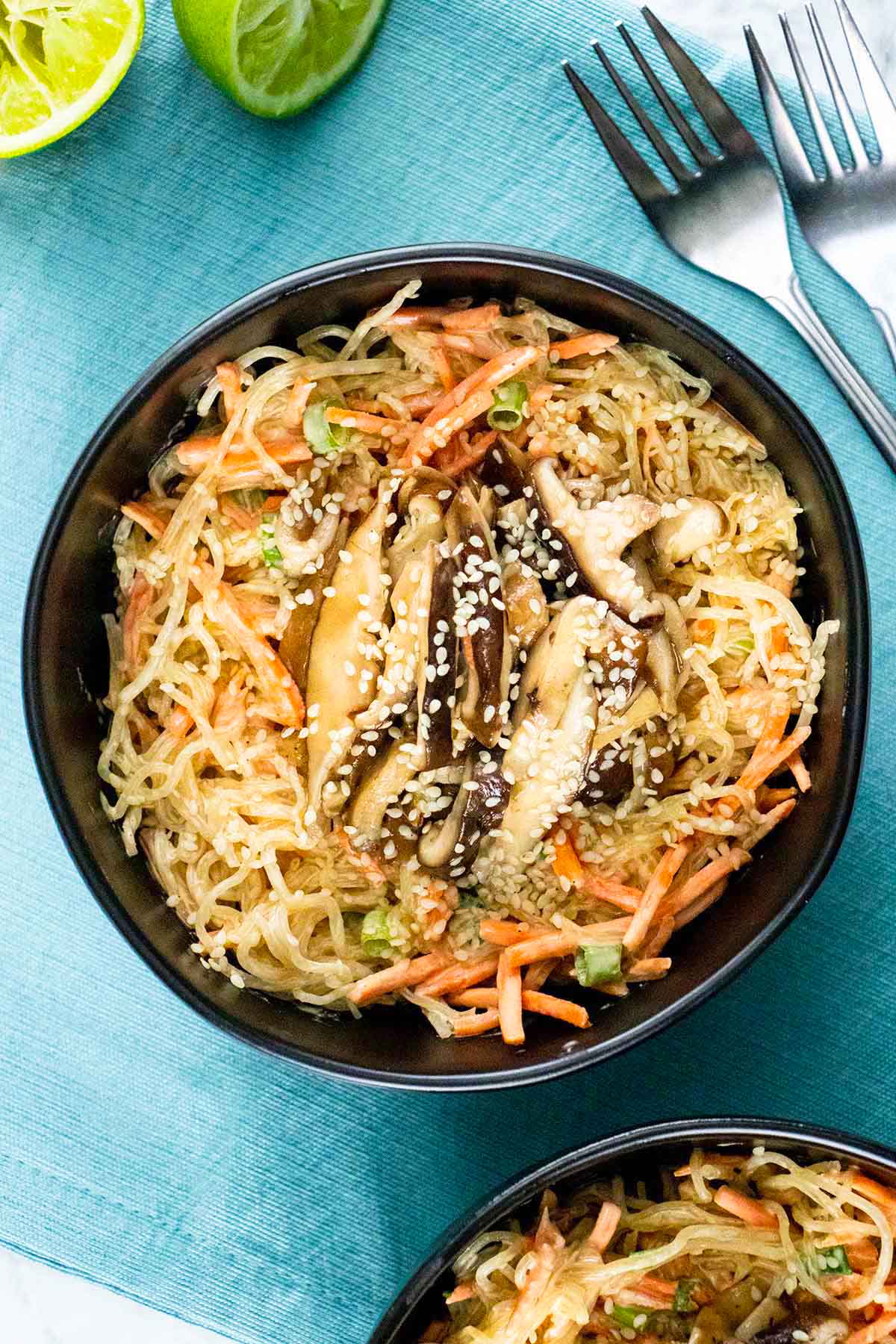 kelp noodle salad with carrots and green onions topped with shiitake mushrooms in a bowl