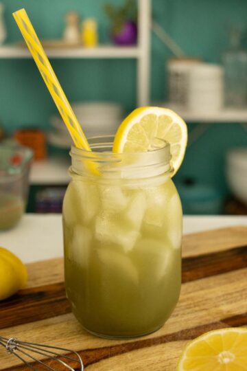 glass of matcha lemonade on a wooden cutting board with a lemon wheel in it