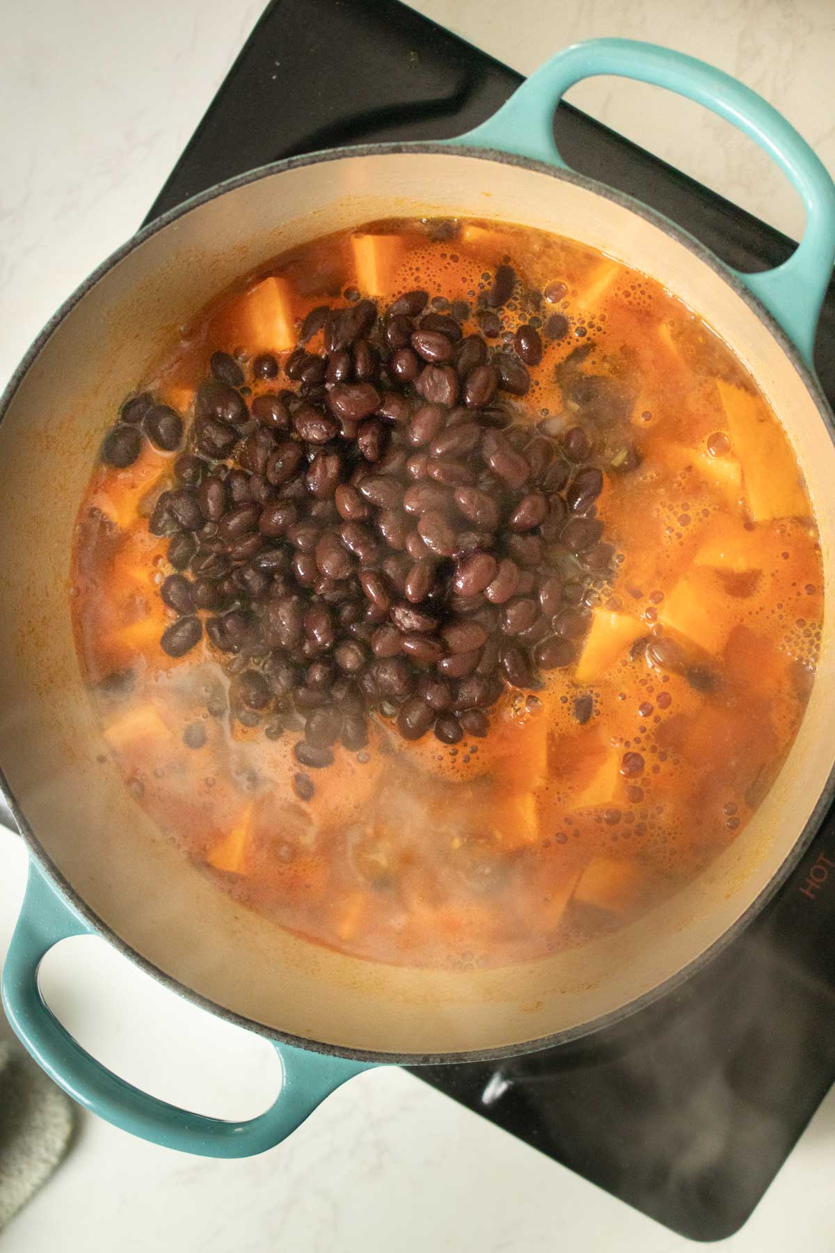 adding the rest of the black bean sweet potato soup ingredients to the pot, boiling