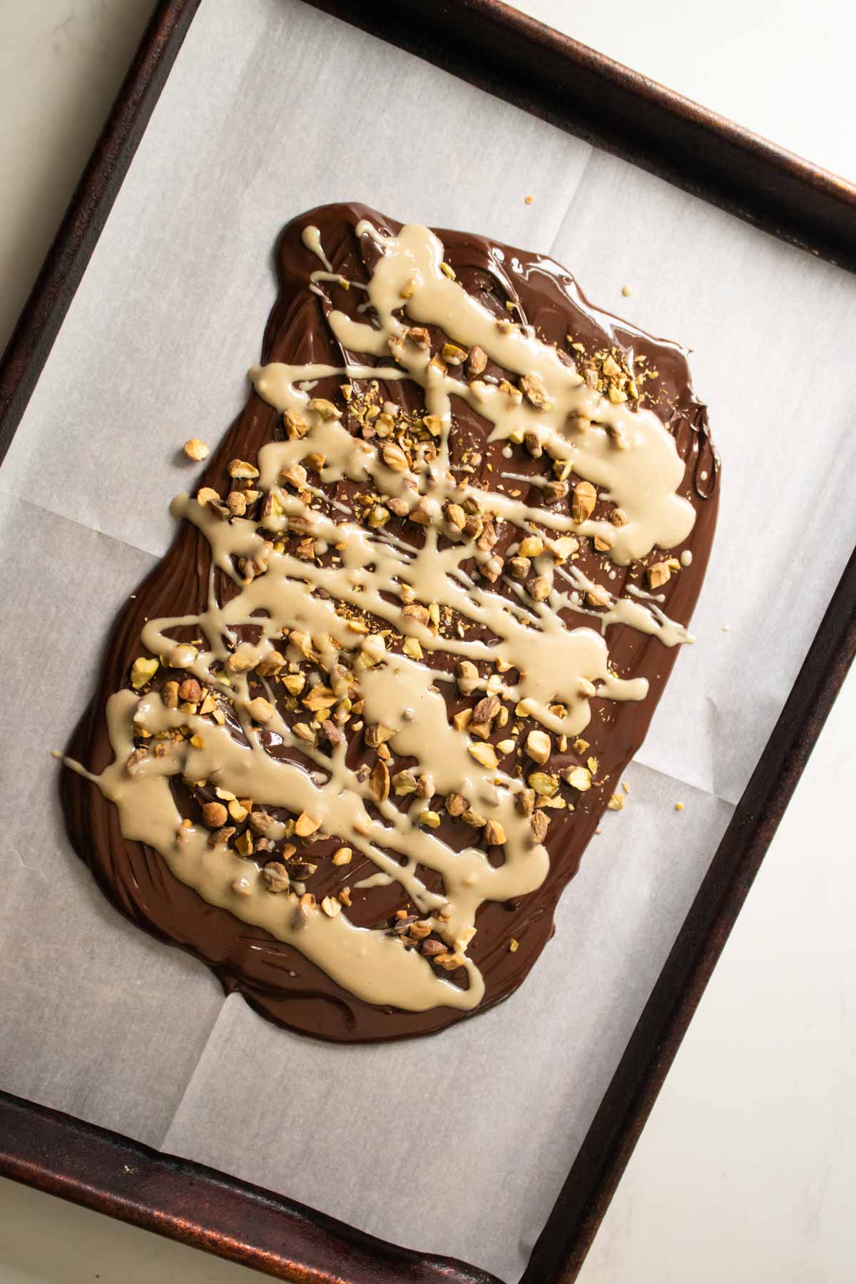 adding the tahini and pistachios to the chocolate on the baking sheet