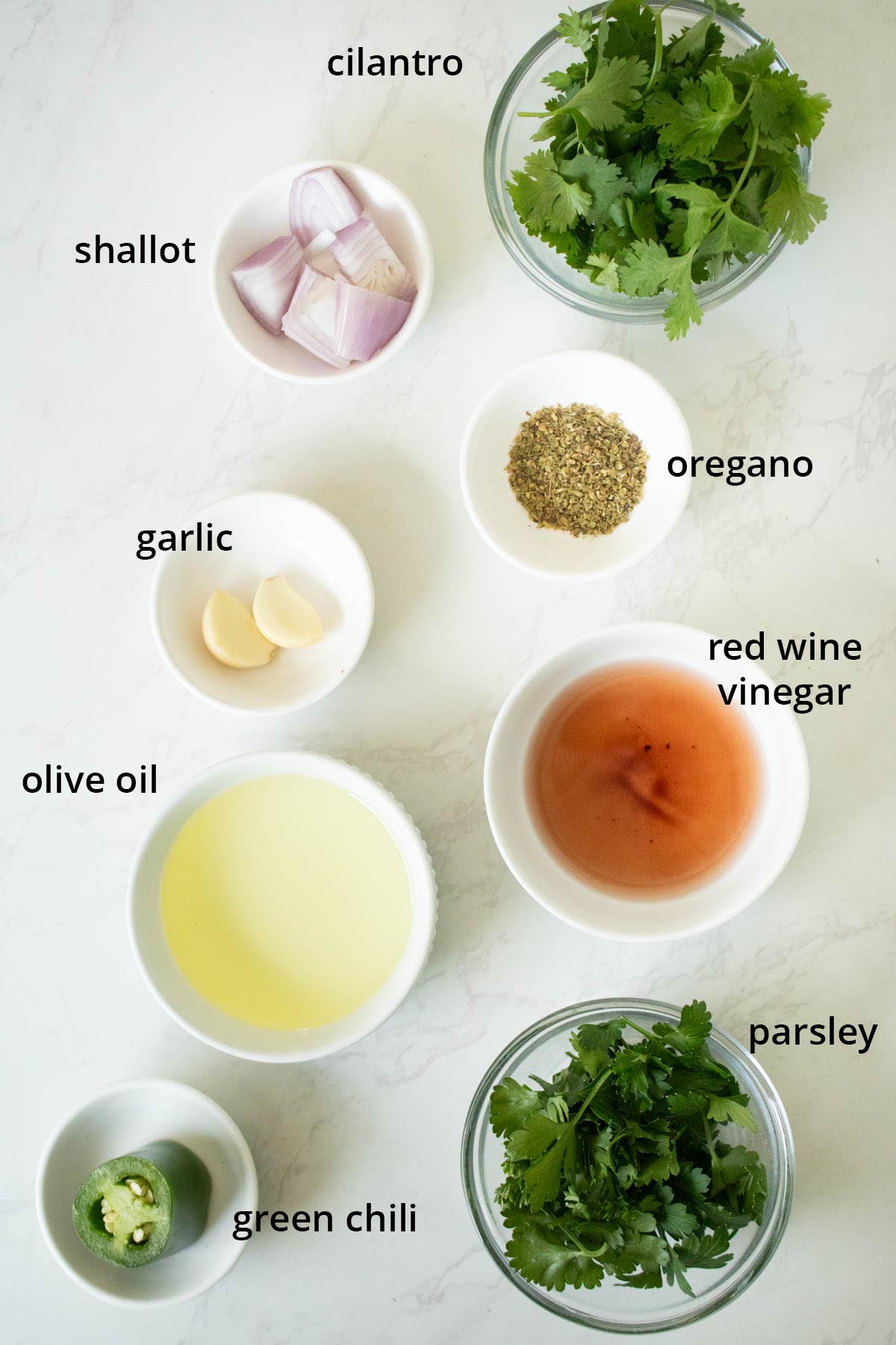 chimichurri ingredients in bowls on a white table, text labels