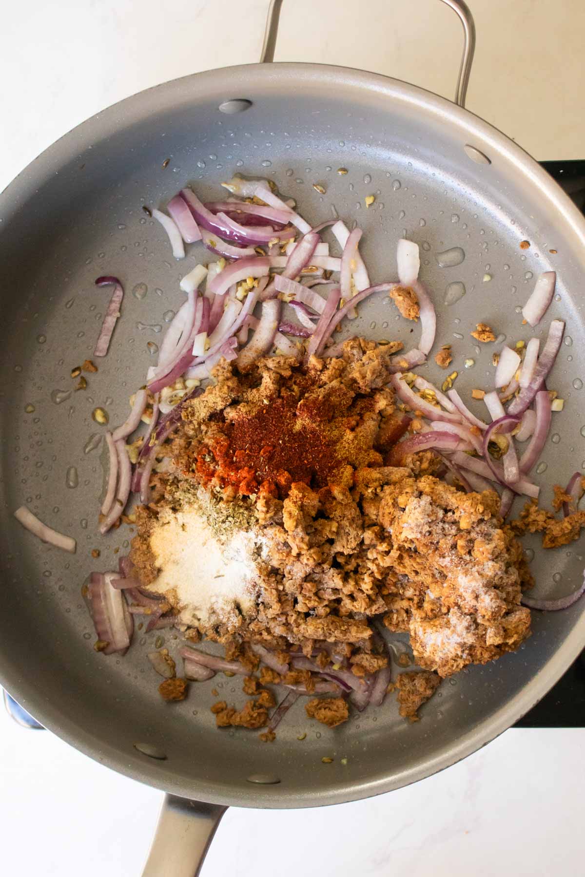 adding veggie grounds and spices to the onion mixture in the pan