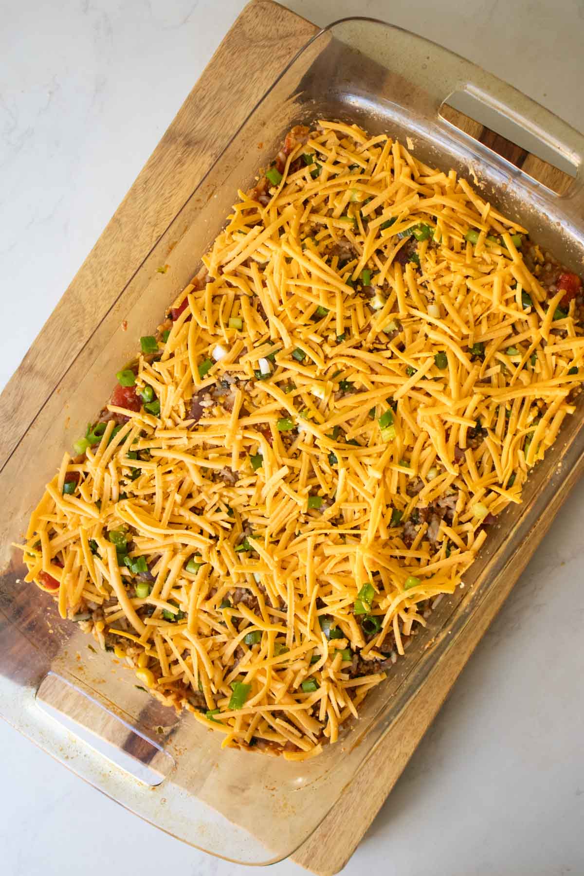 topping the vegan taco casserole with vegan cheddar shreds