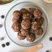 chocolate energy bites in a glass bowl with the mixing bowl and ingredients around it