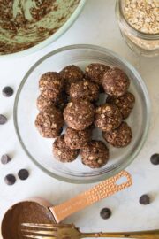 chocolate energy bites in a glass bowl with the mixing bowl and ingredients around it