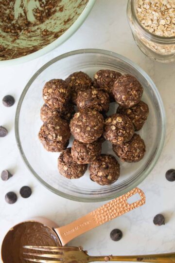 chocolate energy bites in a glass bowl with the mixing bowl and ingredients around it