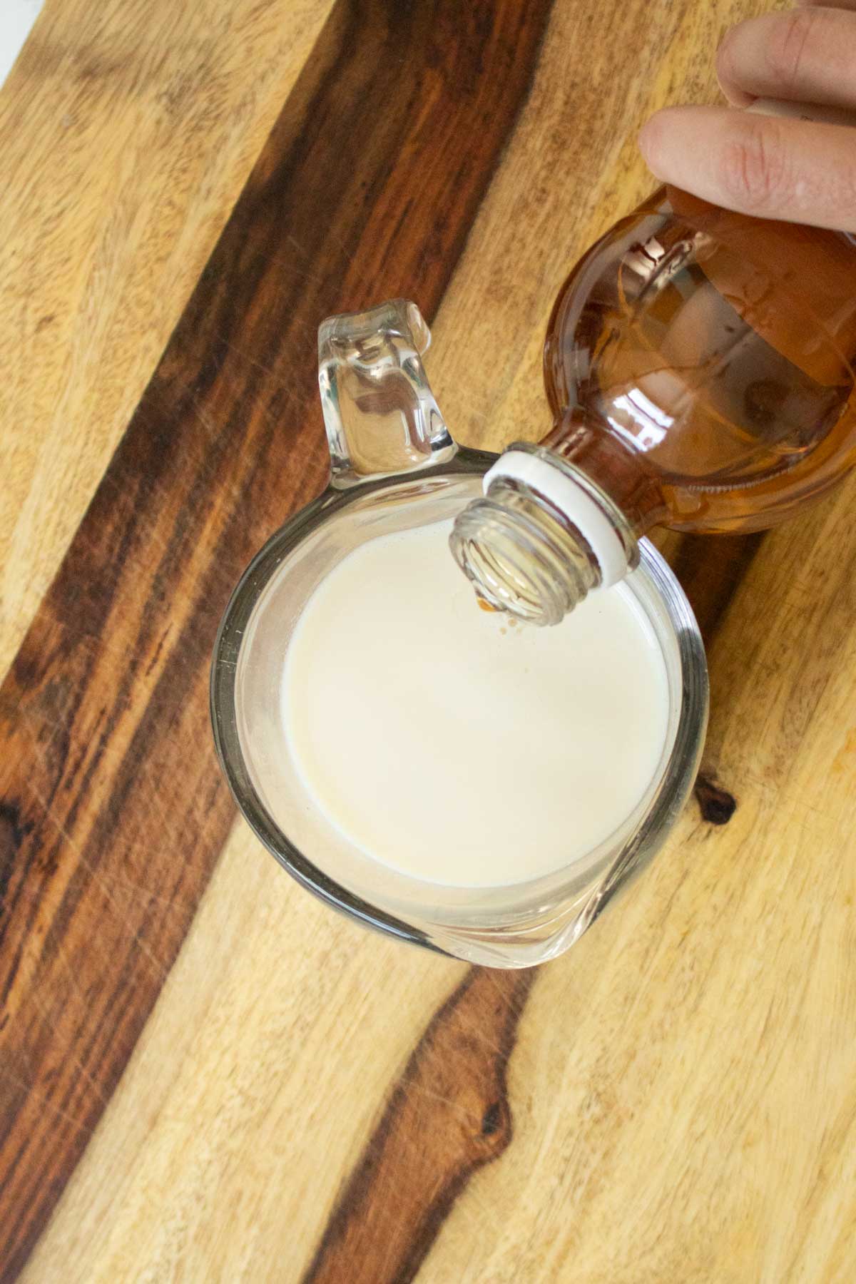 adding apple cider vinegar to soy milk in a measuring cup