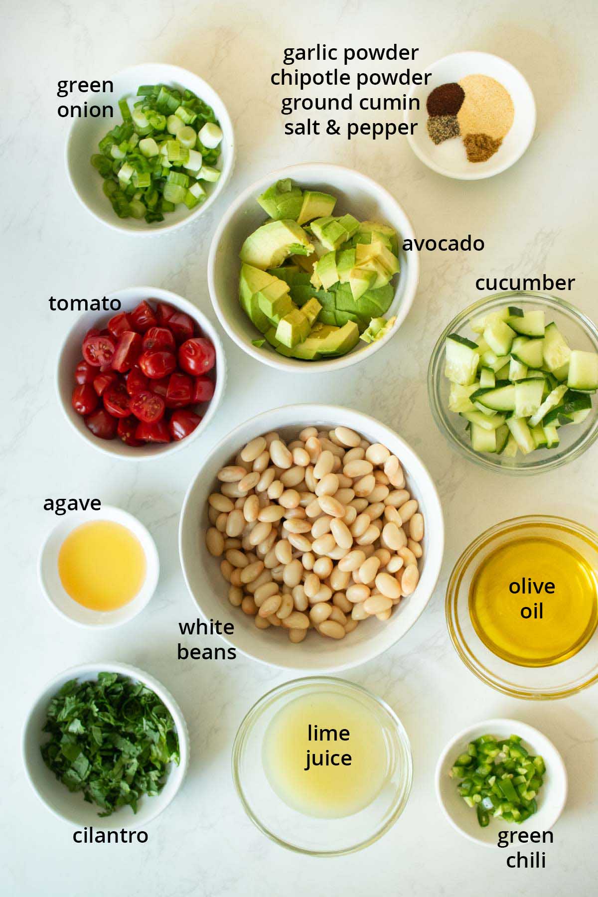 avocado white bean salad ingredients in bowls on a white table, text labels on each one