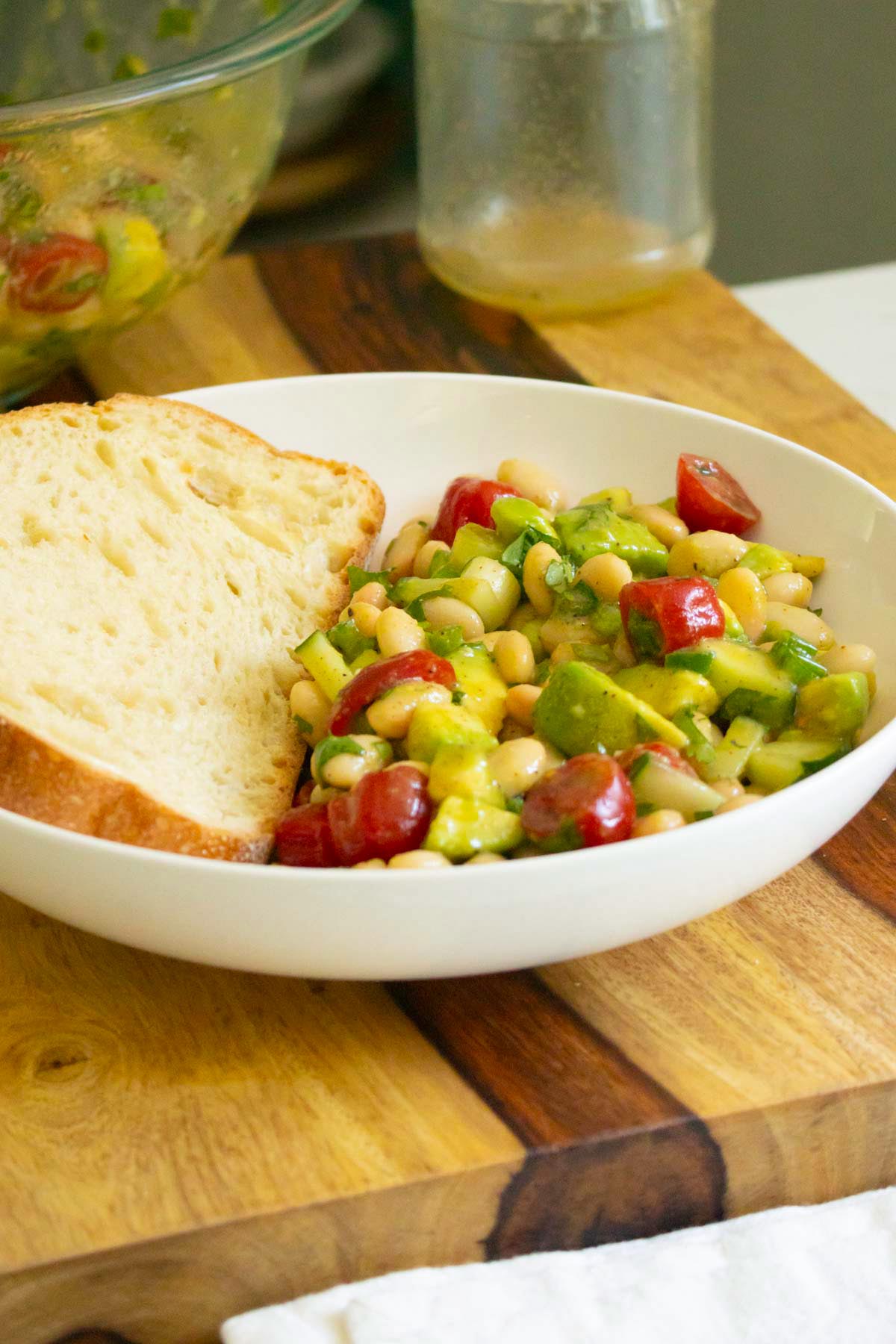 bowl of avocado white bean salad with toast to dip, serving bowl in the background
