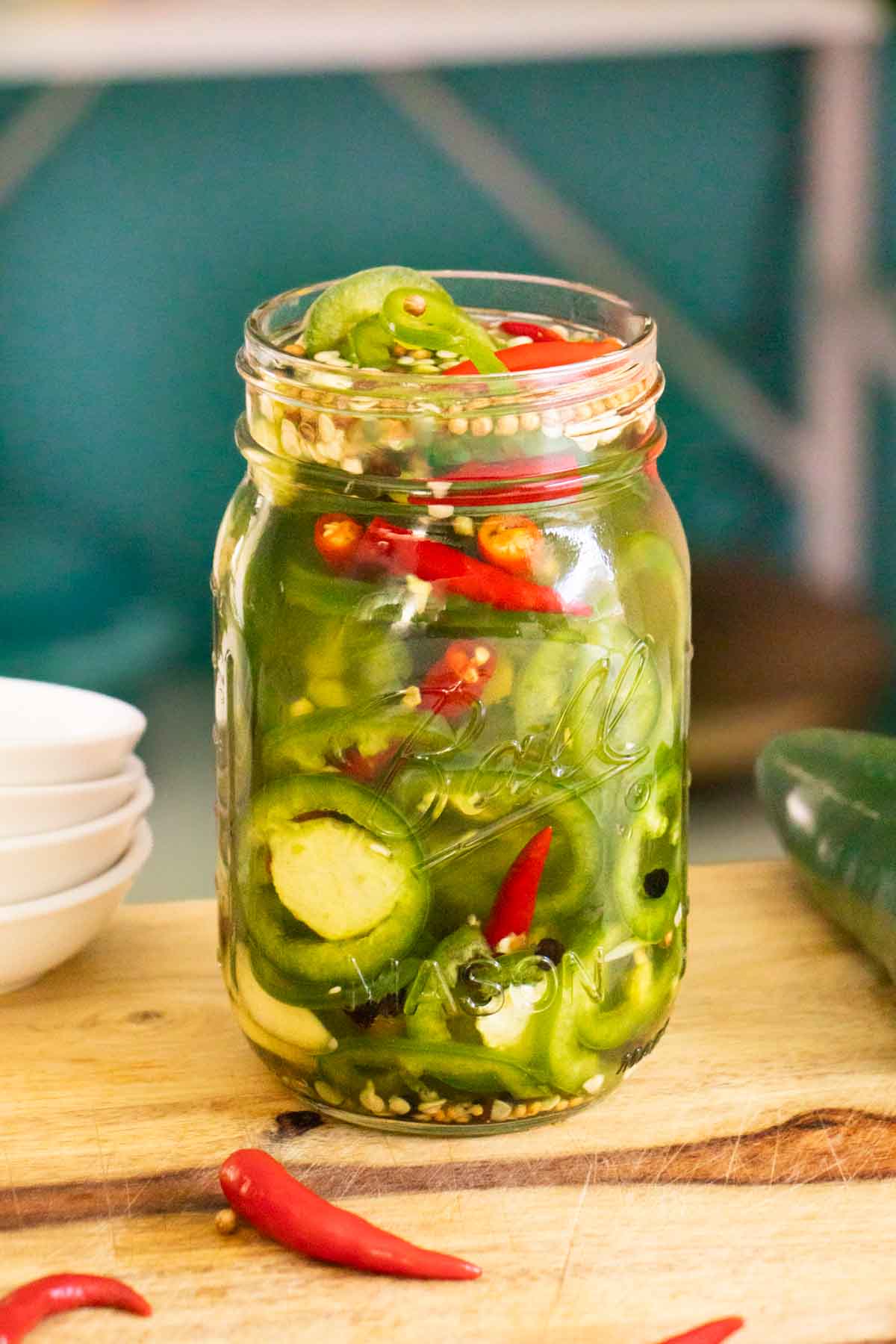 jar of pickled chilies on a wooden cutting board