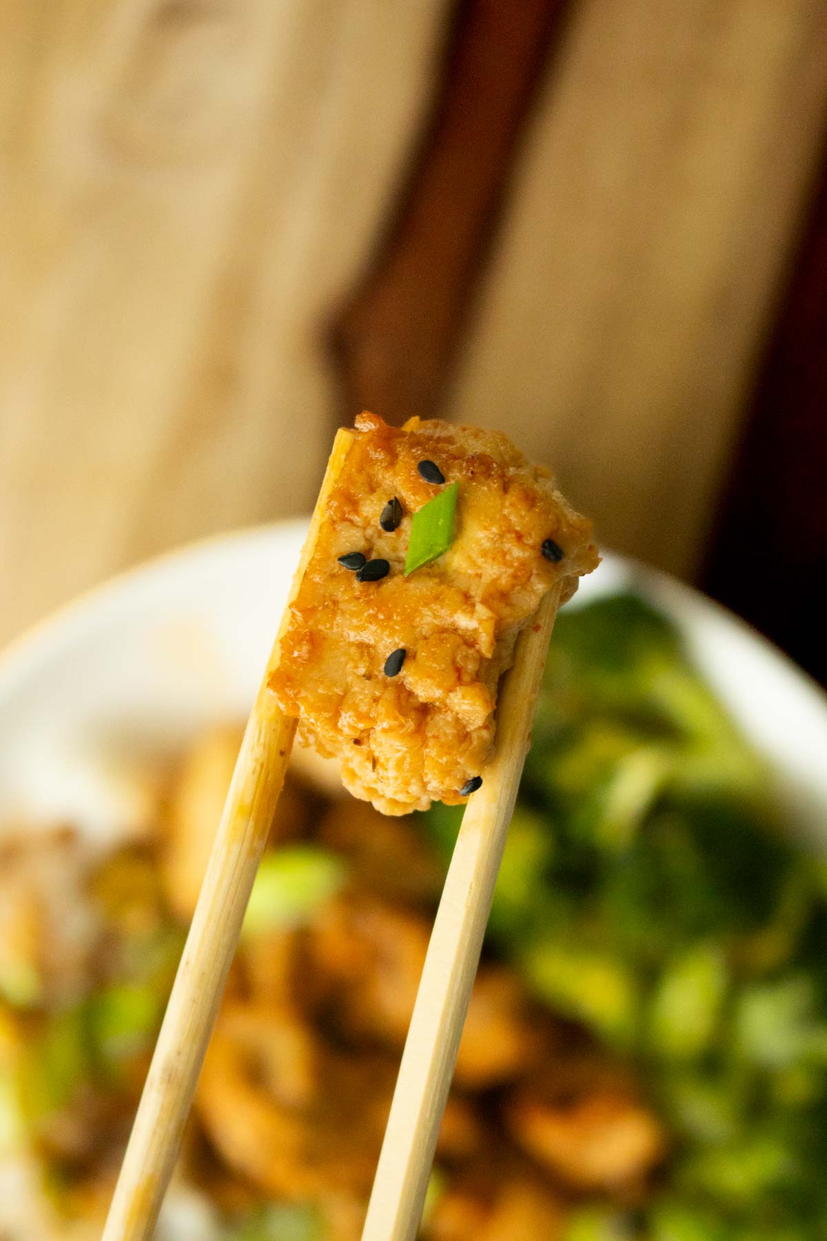 close-up of chopsticks holding a piece of honey garlic tofu