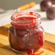 jar of plum freezer jam on a wooden cutting board with plums in the background
