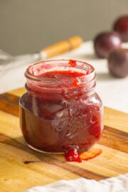 jar of plum freezer jam on a wooden cutting board with plums in the background