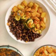 smoky black bean bowls on the counter next to serving bowls of the beans, potatoes, and zucchini