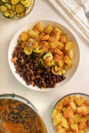 smoky black bean bowls on the counter next to serving bowls of the beans, potatoes, and zucchini
