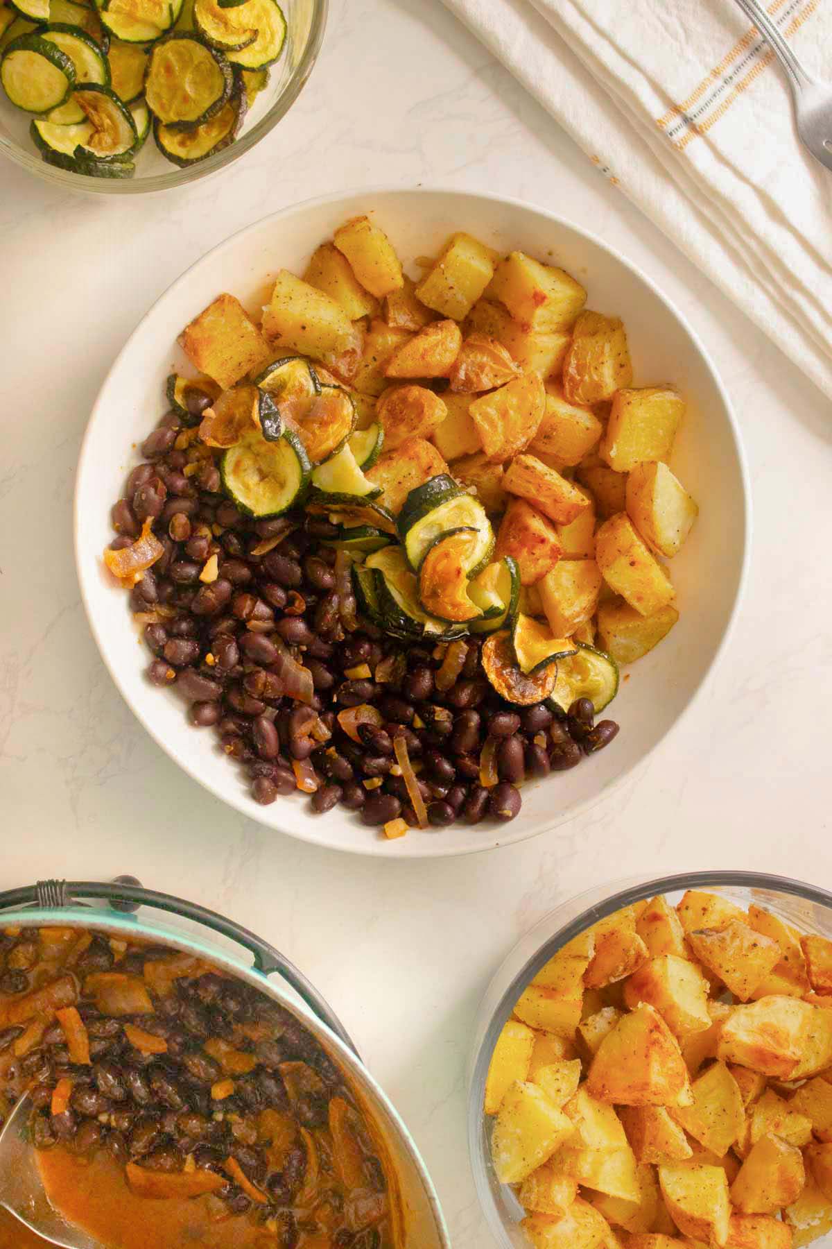 smoky black bean bowls on the counter next to serving bowls of the beans, potatoes, and zucchini