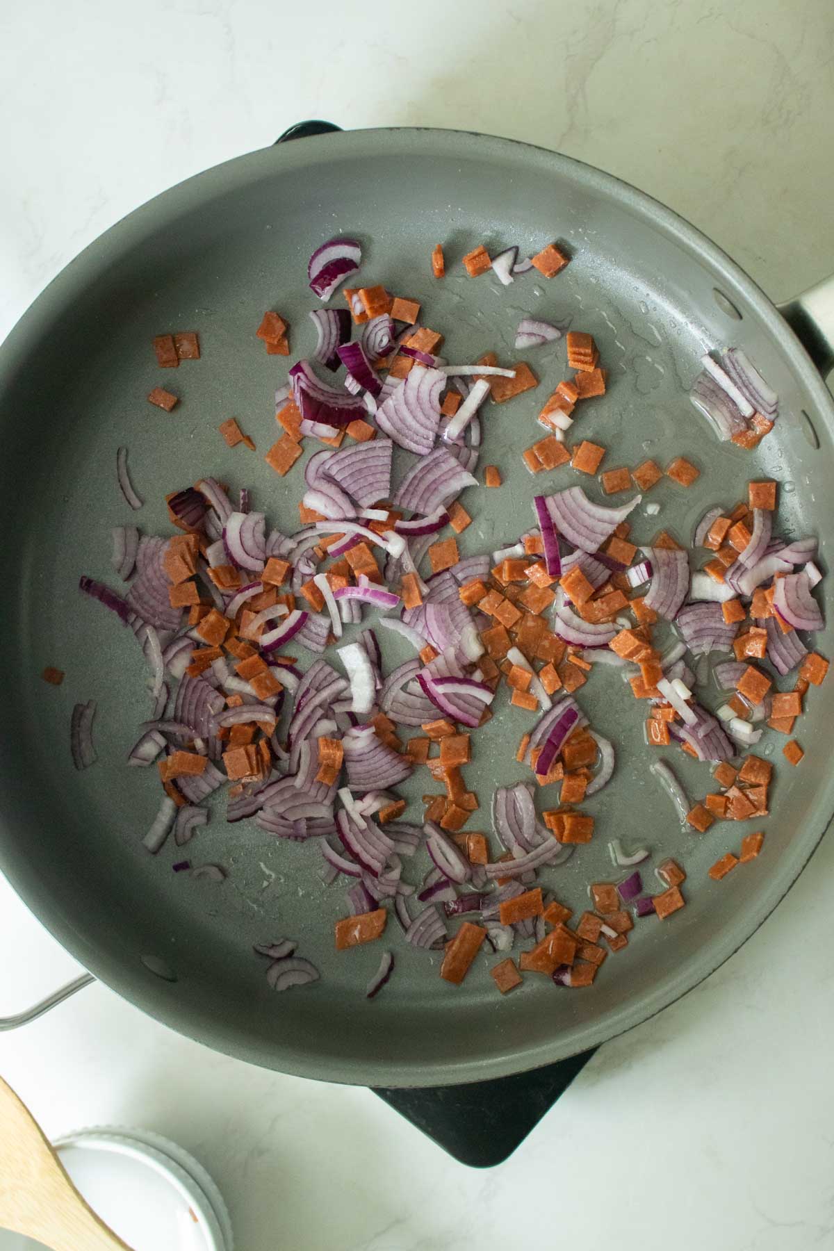 adding onion and vegan bacon to the pan