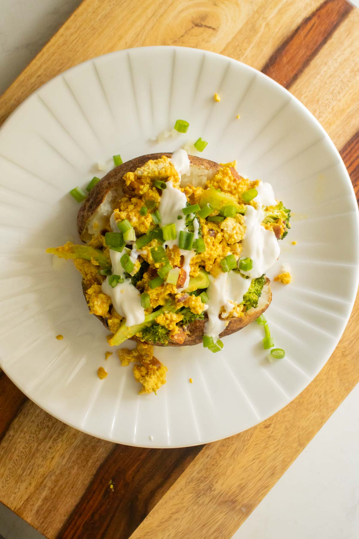adding vegan sour cream and green onion to the loaded baked potato
