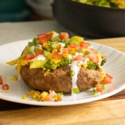loaded baked breakfast potato on a plate with all the toppings, pan of tofu scrambled the background