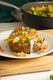 loaded baked breakfast potato on a plate with all the toppings, pan of tofu scrambled the background