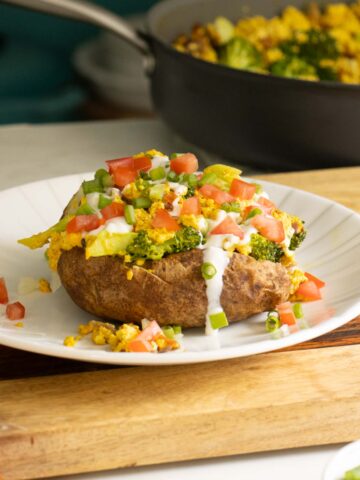 loaded baked breakfast potato on a plate with all the toppings, pan of tofu scrambled the background