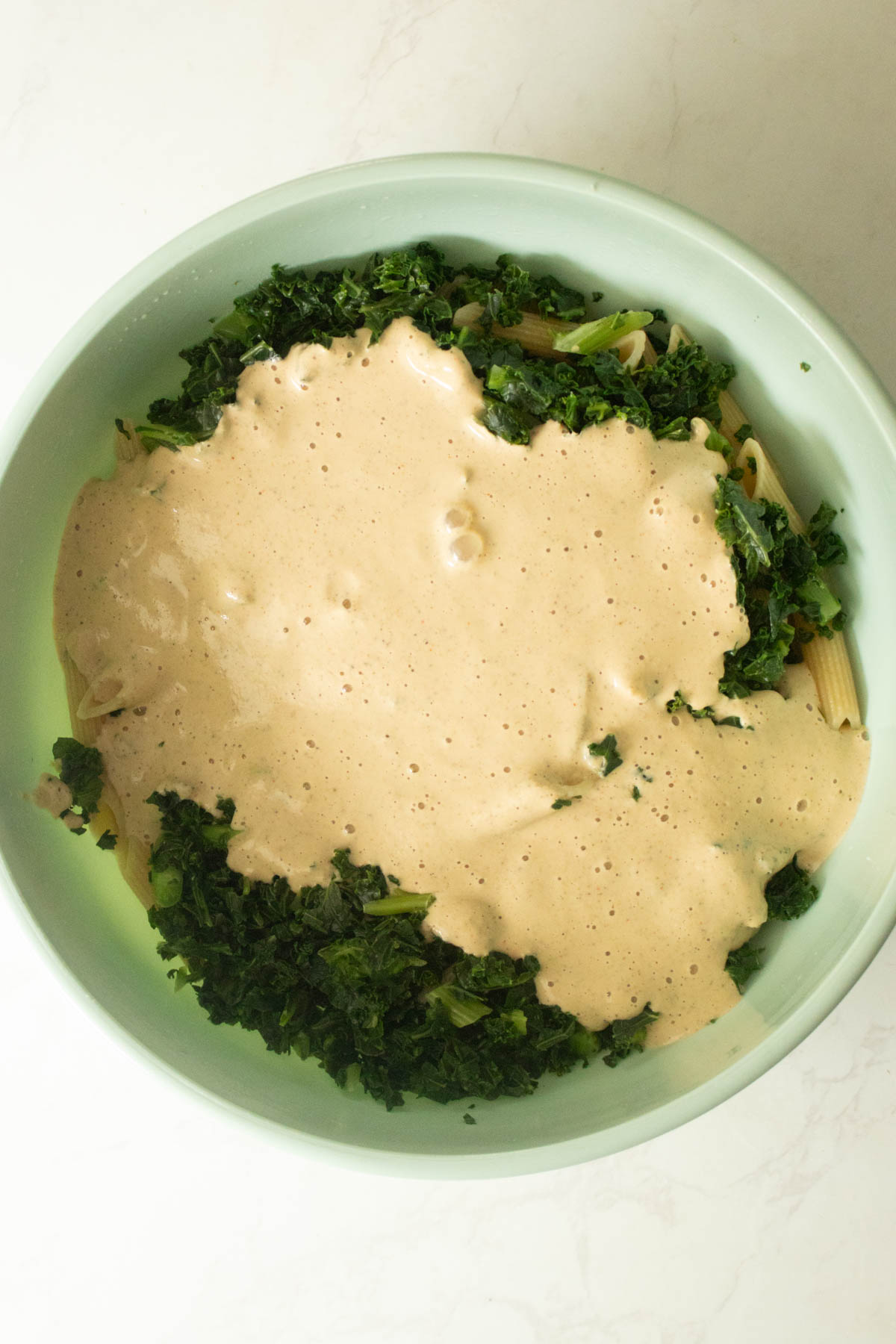 adding the kale and white pasta sauce to the cooked pasta