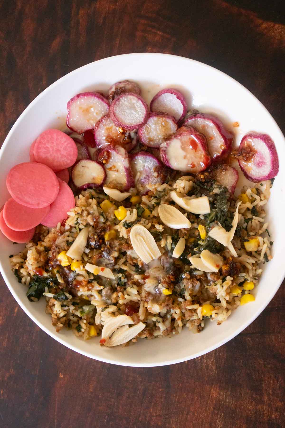 veggie rice bowl with pickled garlic and radishes, sweet chili sauce, chili crisp, and tahini drizzle