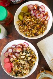 veggie rice bowls with different sauces on a wooden table surrounded by jars of sauces and pickles