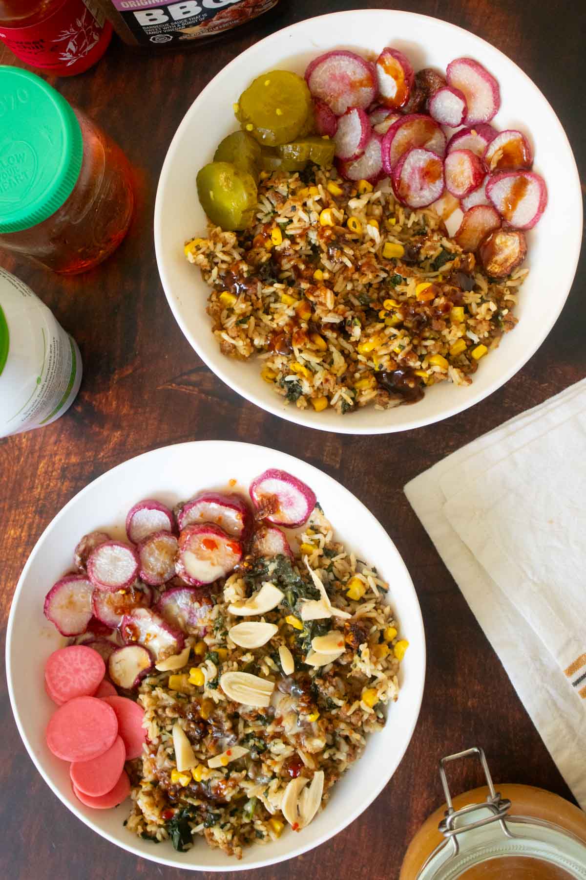 veggie rice bowls with different sauces on a wooden table surrounded by jars of sauces and pickles