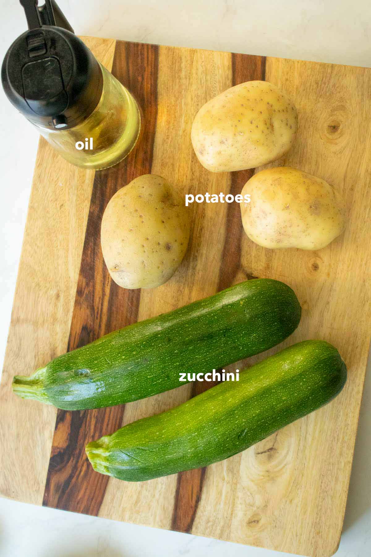 zucchini, potatoes, and oil on the cutting board, text labels on each one
