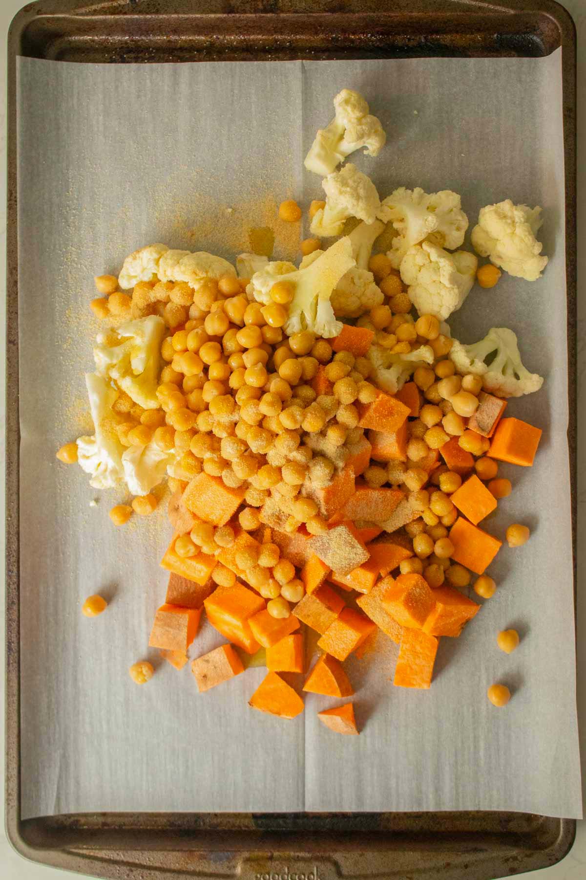 adding oil and spices to the chickpeas and veggies on the baking sheet