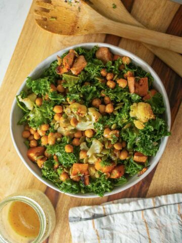 serving bowl of warm kale salad on a wooden cutting board