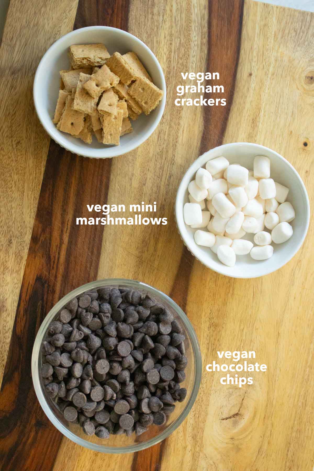 s'mores chocolate bark ingredients in bowls on a wooden cutting board